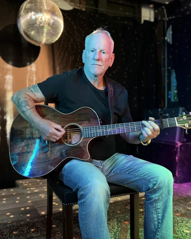 Portræt af Lars Bo Bendixen siddende med guitar, kigger i kameraet